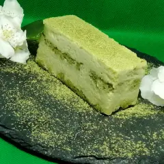 Un delizioso matcha tiramisù, spolverato con polvere verde, adagiato su una pietra scura con fiori bianchi.
