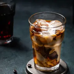 Un bicchiere di **cold brew latte** con ghiaccio, latte e caffè che si mescolano creando un effetto marmorizzato. Sullo sfondo, un altro bicchiere di caffè scuro.