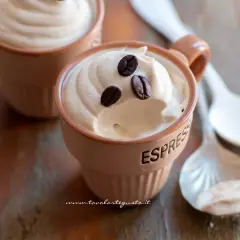Deliziosa ricetta crema caffè con panna, guarnita con chicchi di caffè, servita in tazzine su un tavolo di legno.