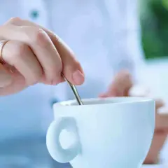 Mano con anello mescola il caffè in una tazza bianca. La scelta è sempre la stessa: caffè con o senza zucchero.