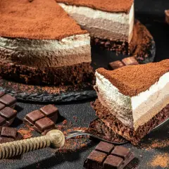 Una golosa cheesecake cappuccino a tre strati, cosparsa di cacao, con pezzi di cioccolato e una fetta servita su una forchetta.