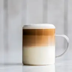 Un bicchiere di caffè macchiato caldo con strati distinti di latte e caffè, sormontato da una schiuma soffice.