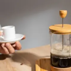 Un uomo tiene una tazzina di caffè mentre una french press caffè è pronta per essere servita.