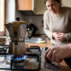 Una donna con mal di stomaco guarda una moka sul fuoco, il caffè è traboccato, un vero caffè bruciato.