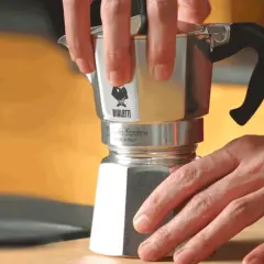 Mani che smontano una moka Bialetti per pulirla dal calcare. Un gesto semplice per un caffè perfetto.