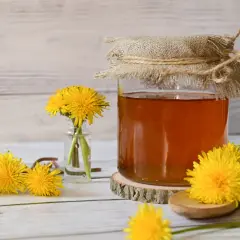 Miele dorato in un barattolo, circondato da fiori di tarassaco. Scopri i tarassaco benefici per la tua salute.