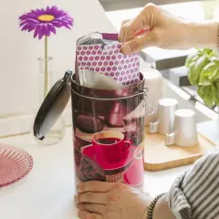 Contenitore decorato per conservare il caffè macinato, con pacchetto di caffè in mano.