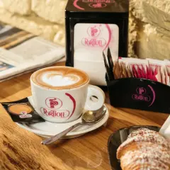 Un cappuccino perfetto con schiuma a forma di cuore, accompagnato da un croissant e un giornale.