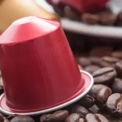 Una capsula di caffè rossa, circondata da chicchi di caffè tostati, pronta per un'esperienza aromatica.