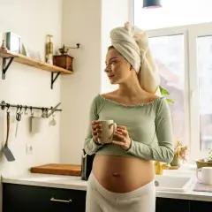 Donna incinta con asciugamano in testa beve una tisana in cucina, un momento di relax in gravidanza.