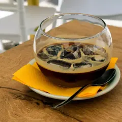 Un bicchiere di caffè freddo con ghiaccio, servito su un piattino con tovagliolo giallo e cucchiaino. Un rinfrescante caffè pugliese per una giornata calda.