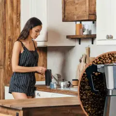 Donna in cucina prepara il caffè, ma la caffettiera non esce caffè. La scena è dominata da chicchi di caffè tostati.