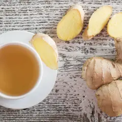 Tazza di tè allo zenzero, con radici e fette di zenzero fresco. Scopri i benefici dello zenzero per il tuo benessere.