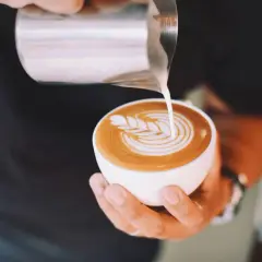 Un barista crea un disegno a latte art su un cappuccino. Latte art: cappuccino prima latte o caffè?