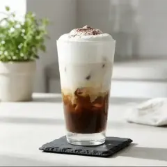 Un bicchiere alto con caffè freddo, latte e schiuma, cosparso di cacao. Ecco come si fa il caffè macchiato perfetto per l'estate.