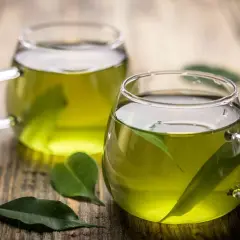 Due tazze di tè verde, con foglie fresche immerse, pronte per gustare le loro proprietà benefiche.