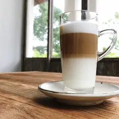 Un macchiatone, un caffè stratificato in un bicchiere trasparente, su un tavolo di legno rustico.