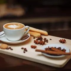 Un delizioso caffè fatto in casa con schiuma a forma di cuore, biscotti, chicchi di caffè e spezie su un tagliere di legno.