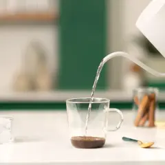 Preparazione di un delizioso spanish latte: acqua calda versata su caffè, cubetti di ghiaccio e un tocco di dolcezza.