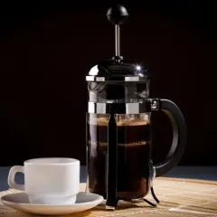 Una tazzina bianca accanto a una caffettiera francese piena di caffè scuro, pronta per essere gustata.