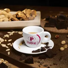 Tazza di caffè fumante, circondata da pezzi di cioccolato fondente, nocciole e pinoli. Un'invitante combinazione di caffè e cioccolato.