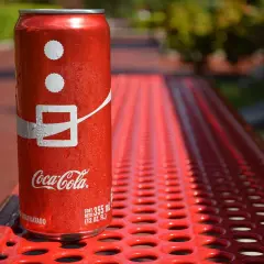 Lattina di Coca-Cola su panchina rossa, con gocce d'acqua. Attenzione, la Coca-Cola fa alzare la pressione!