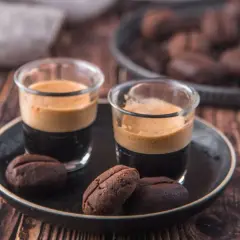 Due bicchierini di espresso con crema e biscotti al caffè moka a forma di chicco, su un piatto scuro.