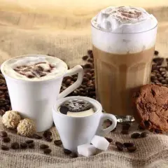 Tre tazze di caffè, una con panna e cacao, un'altra con schiuma e un bicchiere alto di latte cappuccino, accompagnate da biscotti e chicchi di caffè.
