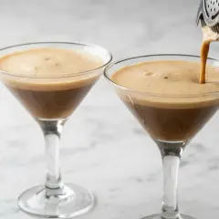 Due bicchieri di caffè shakerato cremoso, uno viene riempito da uno shaker.