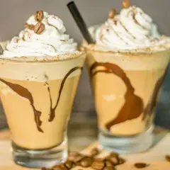 Due deliziosi milkshake al caffè, guarniti con panna montata, chicchi di caffè e sciroppo al cioccolato, pronti per essere gustati.