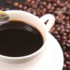 Tazza di caffè decaffeinato, chicchi tostati e zolletta di zucchero su cucchiaino. Ideale per chi vuole godersi il gusto senza preoccuparsi della pressione.