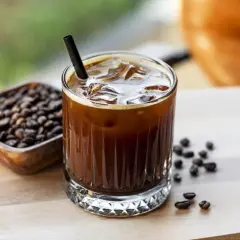 Un bicchiere di caffè freddo, con ghiaccio e cannuccia, accanto a chicchi di caffè. Ecco cos'è il cold brew: una bevanda rinfrescante.