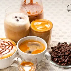 Varietà di deliziosi caffè italiani: un espresso, un cappuccino decorato, un caffè macchiato e un frappé. Chicchi di caffè tostati completano la scena.