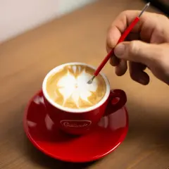 Un barista crea disegni sul cappuccino con uno strumento, mostrando come fare latte art.