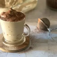 Deliziosa cremina caffè in una tazza di vetro, spolverata di cacao. Accanto, un colino per dolci e un barattolo di caffè.