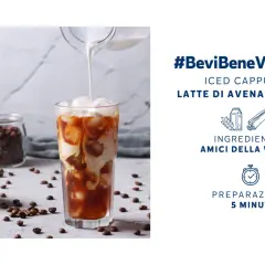 Un rinfrescante cappuccino di avena freddo versato in un bicchiere con ghiaccio, circondato da chicchi di caffè e cannella.