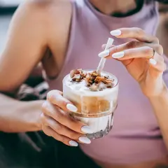 Mani con unghie bianche sorreggono un bicchiere di delizioso **caffè freddo** con topping croccante.