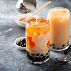 Due bicchieri di bubble tea con perle di tapioca. Un bicchiere è in preparazione con latte versato su un tè arancione.