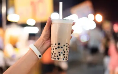 Un bicchiere di bubble tea con perle nere, tenuto da una mano con un braccialetto bianco. Un sorso di freschezza che ricorda le sue origini asiatiche.