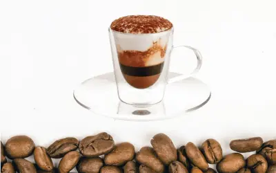 Un bicerin coffee a strati in una tazza di vetro, con cacao in polvere in cima e chicchi di caffè tostati sul fondo.