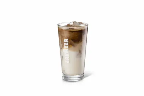 Un bicchiere alto di iced latte Lavazza con cubetti di ghiaccio e striature di caffè e latte.