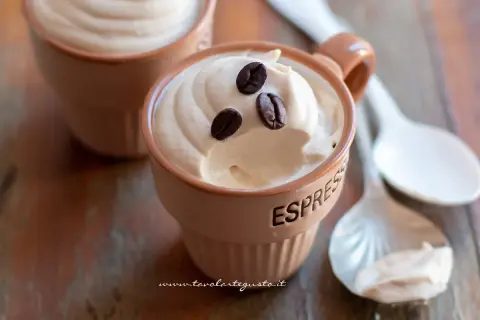 Deliziosa ricetta crema caffè con panna, guarnita con chicchi di caffè, servita in tazzine su un tavolo di legno.