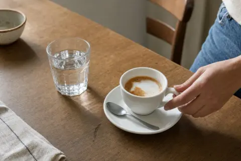 Una mano afferra una tazza di cappuccino su un tavolo di legno. Ti chiedi quante calorie ha un cappuccino?