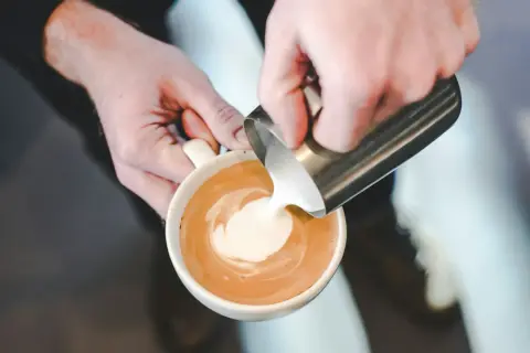 Barista versa latte montato in una tazza di caffè, creando un disegno a spirale.