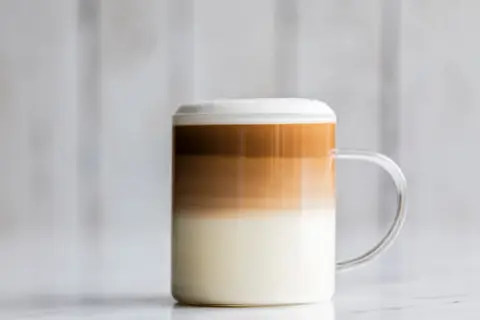 Un bicchiere di caffè macchiato caldo con strati distinti di latte e caffè, sormontato da una schiuma soffice.
