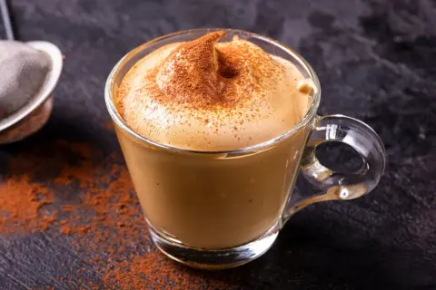 Una tazza di crema di caffè fatta in casa, spolverata di cacao, su uno sfondo scuro.