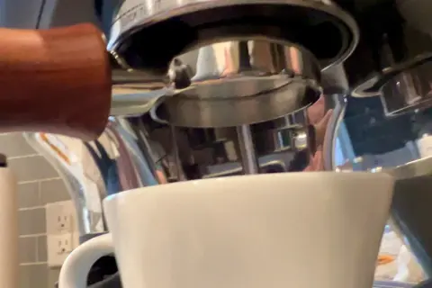 Manuale per capire come mettere le cialde nel portafiltro, con una tazzina bianca pronta a ricevere l'espresso.