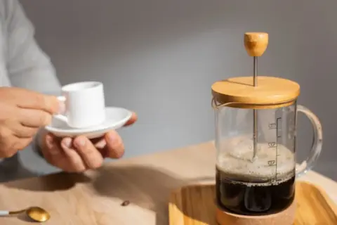 Un uomo tiene una tazzina di caffè mentre una french press caffè è pronta per essere servita.
