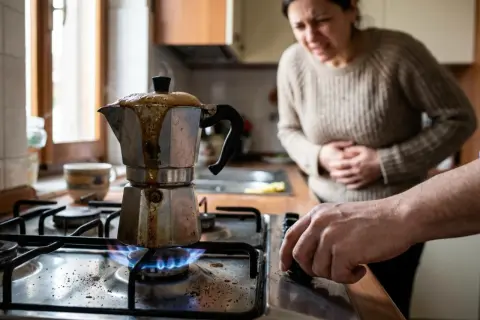 Una donna con mal di stomaco guarda una moka sul fuoco, il caffè è traboccato, un vero caffè bruciato.