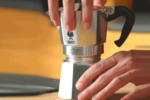 Mani che smontano una moka Bialetti per pulirla dal calcare. Un gesto semplice per un caffè perfetto.